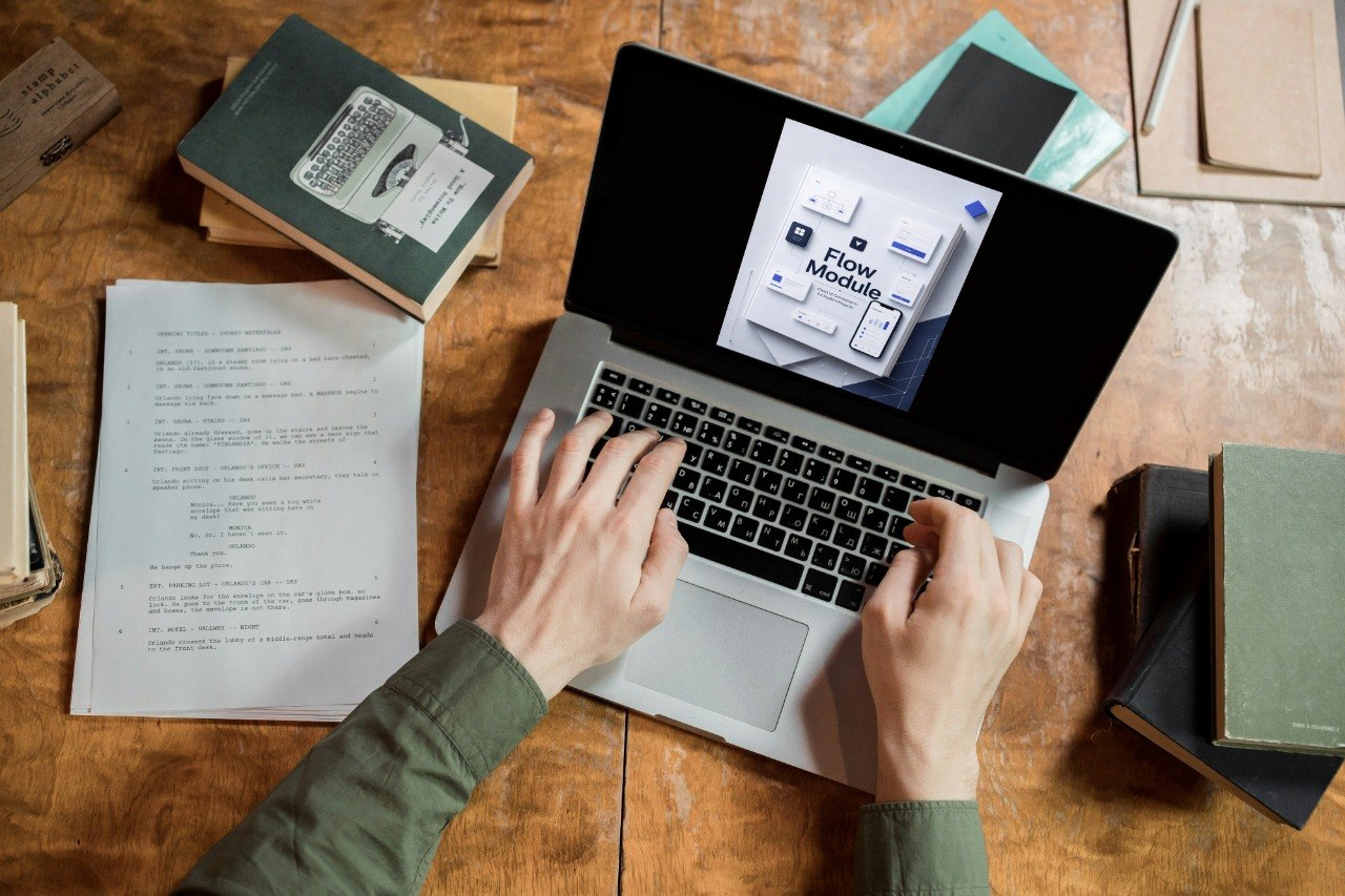 Person using a laptop on a wooden desk with books and papers.